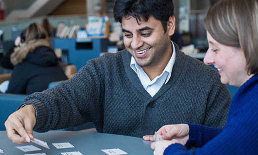 A man and a woman sit at a round table. They are smiling and playing cards. 