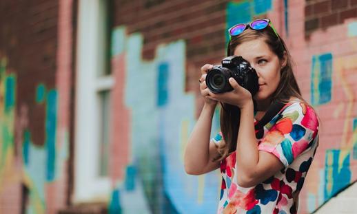 An NSCC photography student taking a photo while standing in front of a wall covered in graffiti.