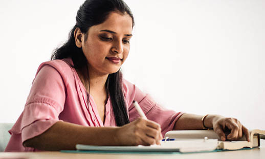 A woman sits at a desk and writes in a notebook.