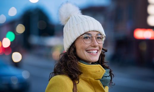 Young woman with winter hat and glasses smiling.