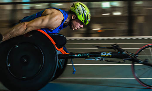 A man in a racing wheelchair is racing around a track. 
