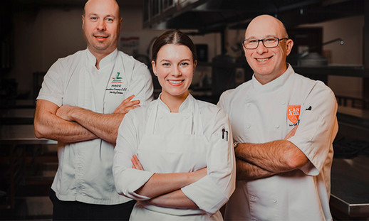 Three faculty in white are seen with their arms folded smiling at the camera.