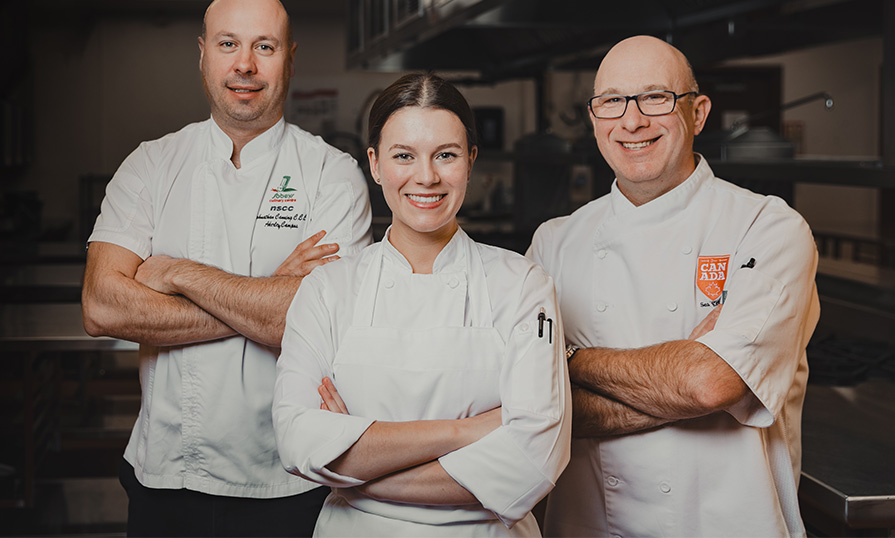 Three faculty in white are seen with their arms folded smiling at the camera.