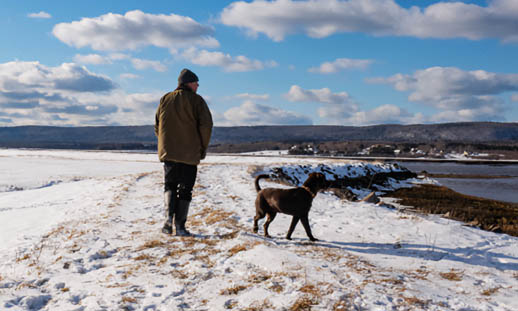 A man and a dog walk down a snowy shoreline.