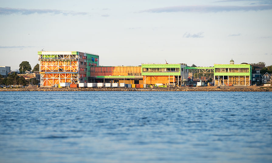 NSCC's Sydney Waterfront Campus is pictured. It is under construction. Four people are seen walking towards a section of the building. They are wearing reflective vests and hardhats.