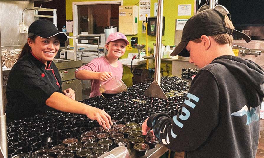 Employee in the kitchen filling containers with the help of two children volunteers