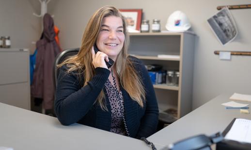 A woman sits at a desk in an office on the phone.