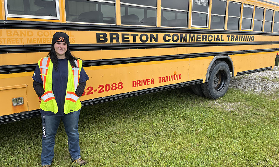 Ellen wears a safety vest and stands in front of a yellow school bus.