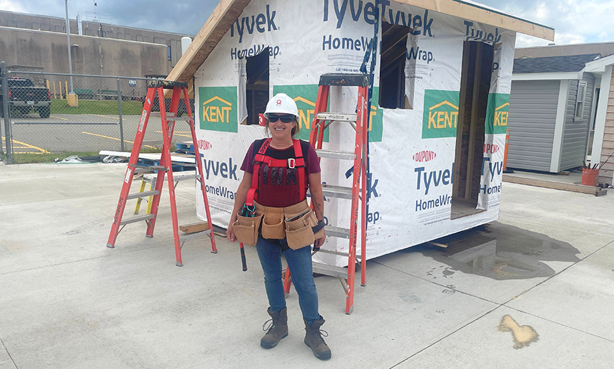 Melanie wears protective gear and stands in front of an under-construction shed.