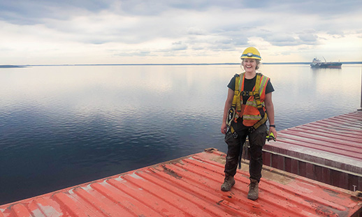 Olivia stands atop a red shipping container on the deck of a ship.