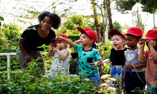 An Early Childhood Education teacher showing a group of children something in a garden.