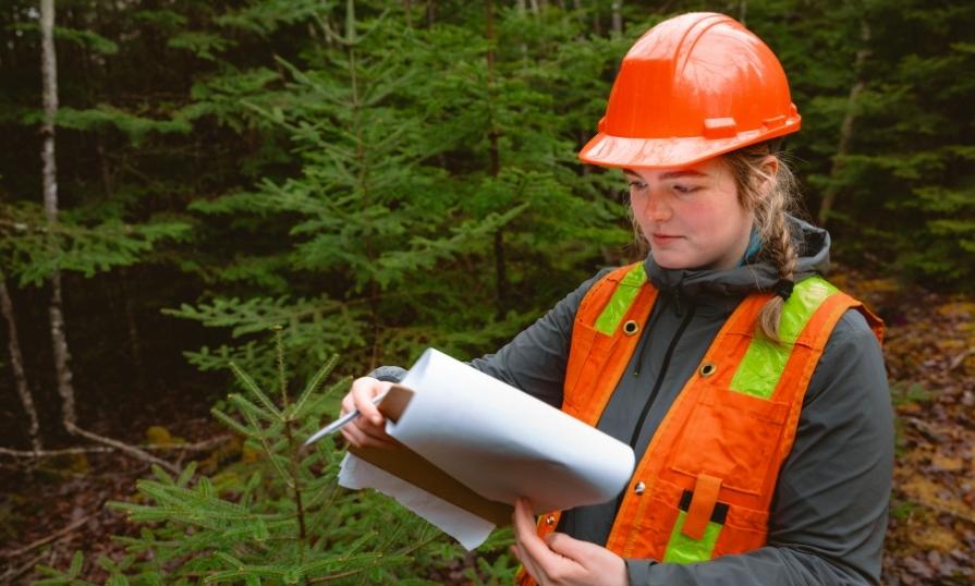 An NSCC NRET student in the forest checking a notebook