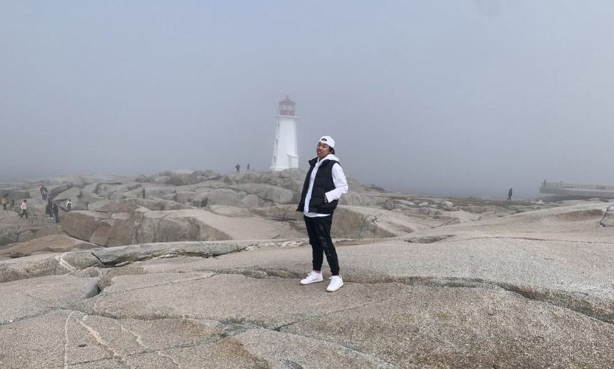Gabe stands on the rocks with the Peggy's Cove Lighthouse behind him.