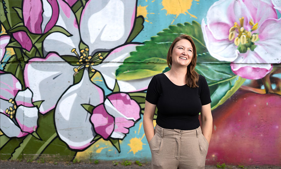 Genevieve Allen-Hearn is pictured. She is standing in front of a mural.