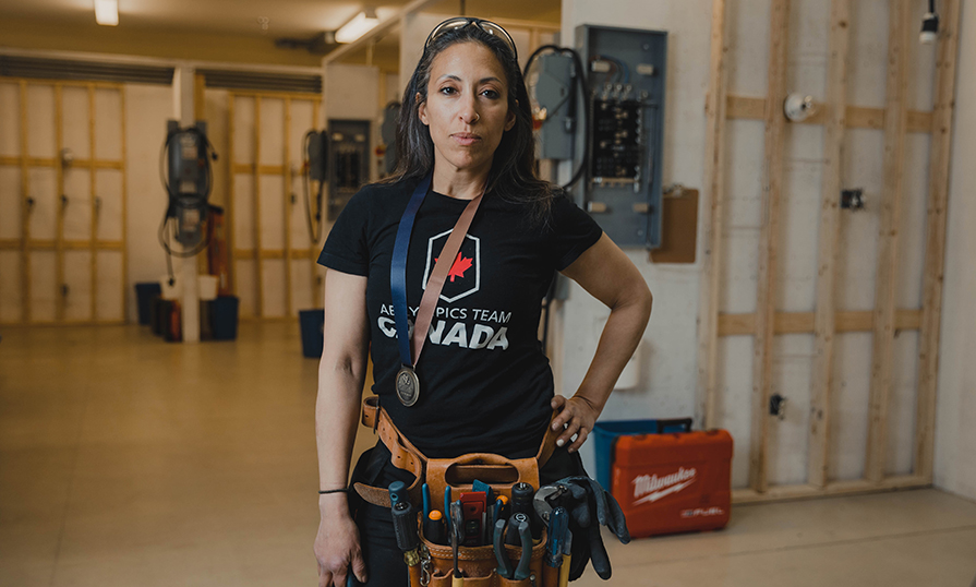 A person standing in an electrical shop wearing a bronze medal around their neck.