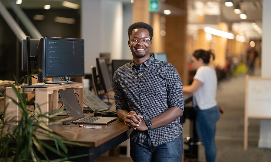 Sandrico Provo leaning against a standing desk in his office.