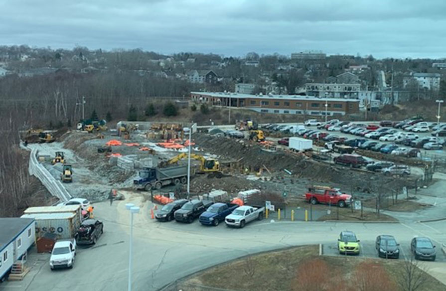A construction site near a busy parking lot continues as the foundation begins to be poured. 