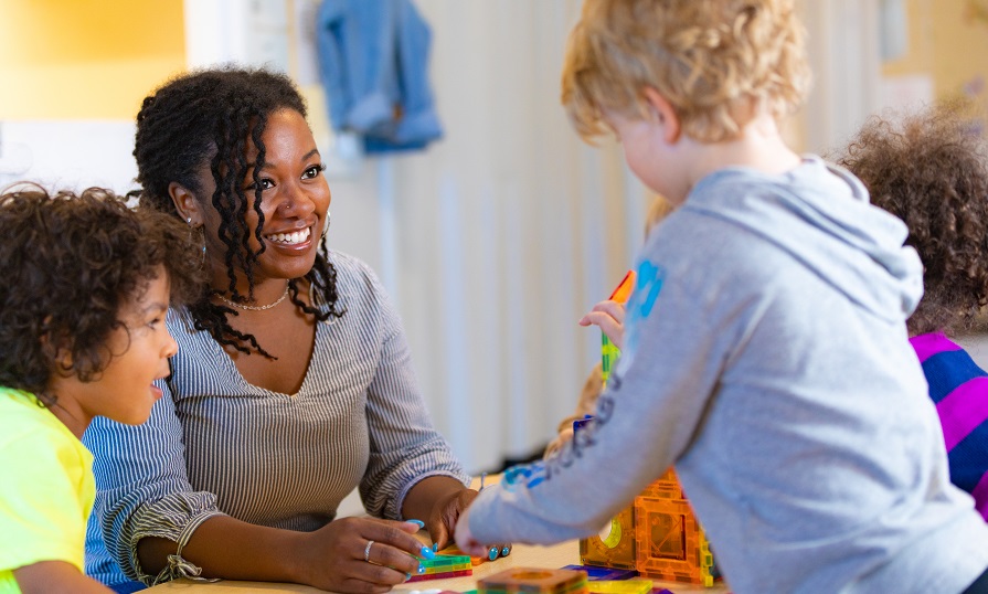 A woman and a young girl play at a table. They are smiling.