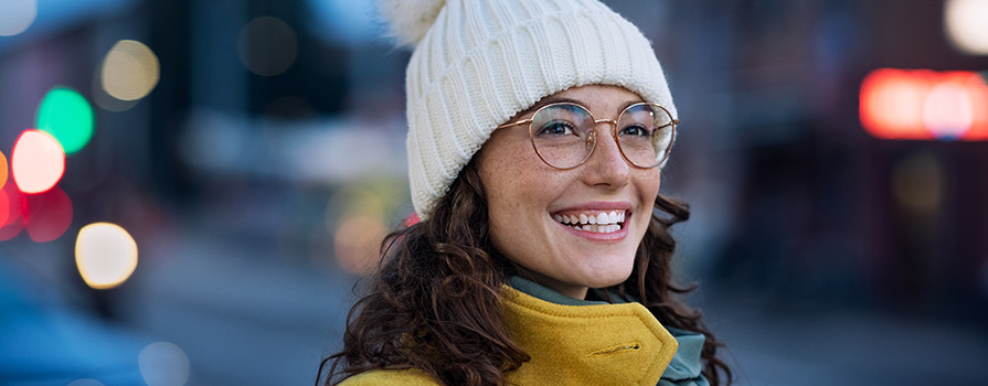 Young woman with winter hat and glasses smiling.