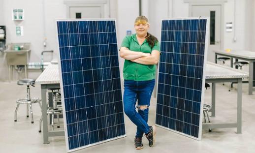 Woman standing crossed armed smiling between two large solar panel in a classroom setting. 