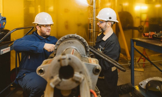 Two people working on a large pipe in a workshop.