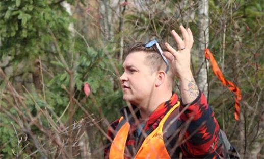 NSCC faculty member Nik Phillips lists his hand while standing in the woods