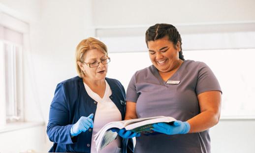 Two women in scrubs look at an open folder.
