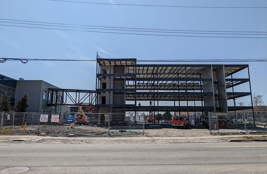 From a street view, the frame of a student housing project is fenced in as progress continues.