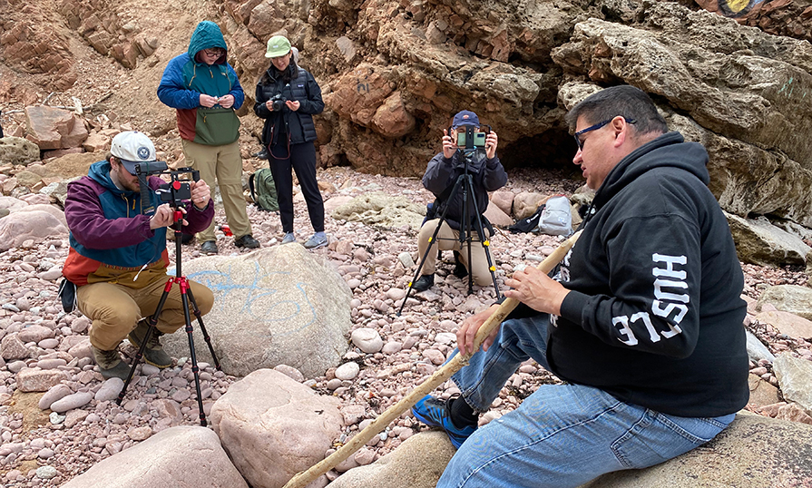 A group of people people taking videos with their phone of someone presenting in a cave.