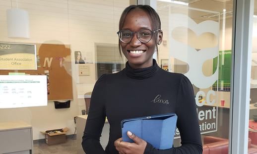 Ribi, a young woman from Kenya, stands in front of the glass walls of the NSCC Student Association offices.