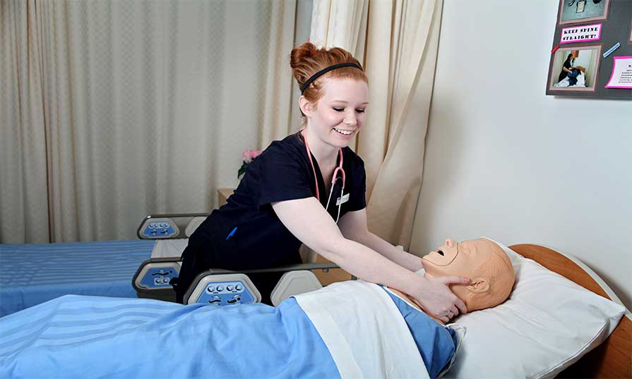 Nursing student standing next to simulated patient while providing care