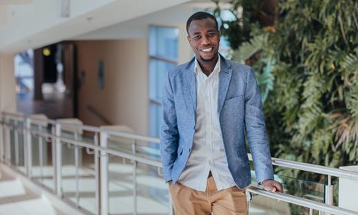 Mashud Zebo, an NSCC graduate, stands in front of the green wall at Institute of Technology Campus and smiles.