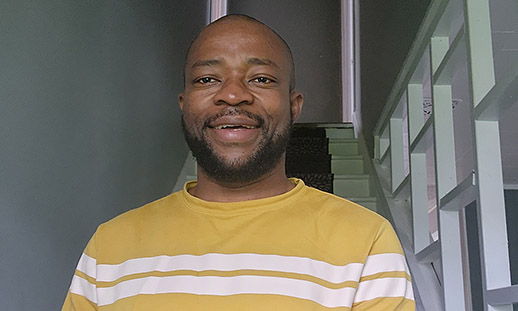 Nduka, wearing a yellow sweater, smiles at the camera.