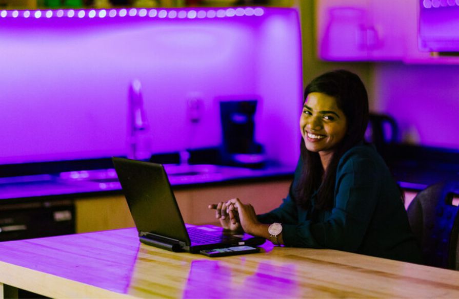 Smiling woman sitting in an innovative workspace, focused on her laptop as she works.