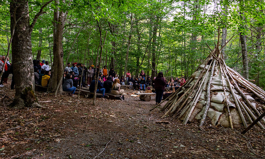 Tourism students gather in wooded area next to a wigwam at Kejimkujik National Park