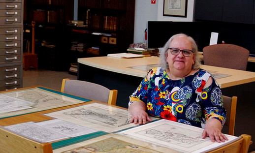Woman librarian sitting at desk with historical maps placed in front of her