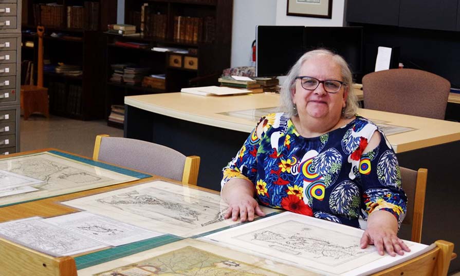 Trish Leblanc sitting at a desk with historical maps laid out in front of her