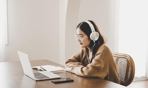 Young woman sitting at a desk with headphones watching a session on her laptop.