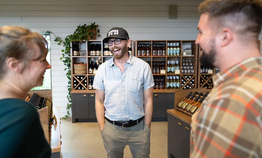 Jeremy Novak, owner of Where It’s At Tours, is pictured. He is talking to two people in the foreground. In the background, wine is shown.