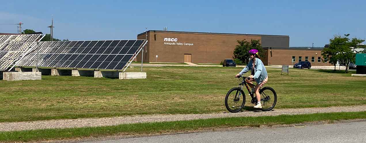 Image of a person in a pink helmet riding a bicycle in a path in front of Annapolis Valley Campus
