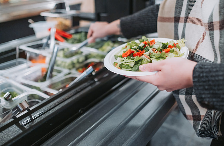 Picture of a garden salad being made at a salad bar. 