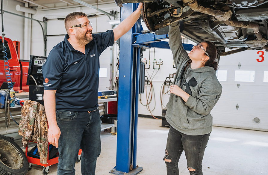 A faculty and student look under a raised car.