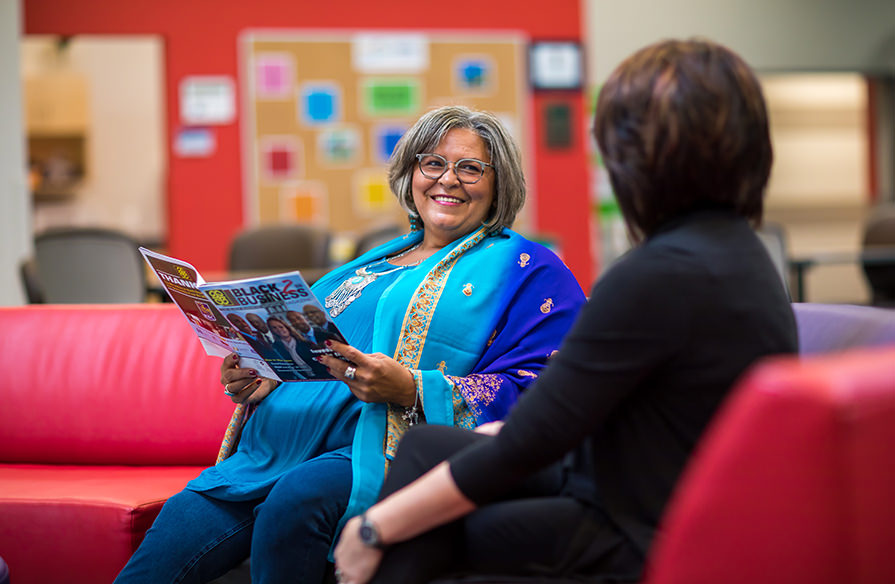 Two women sit smiling on a couch together.