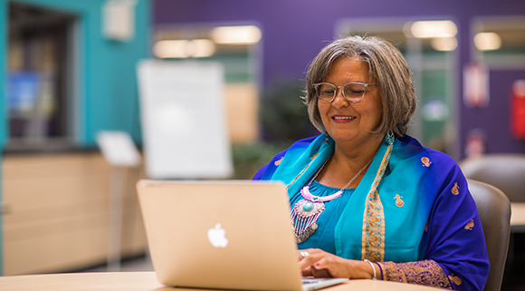 Woman in bright blue dress sits smiling at her laptop in the Digby Learning Centre.