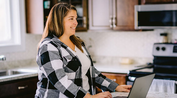 A student standing and looking at a laptop screen in a kitchen.