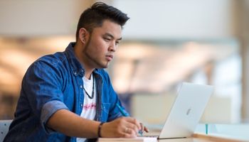 An NSCC student sits in a campus learning space using a laptop.