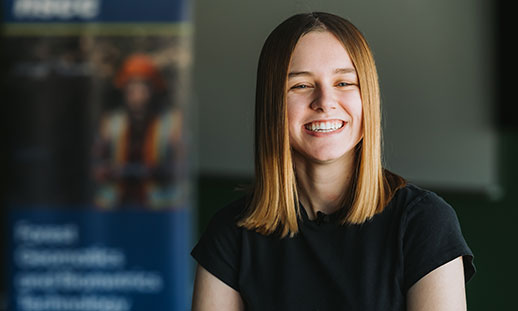 A student with long brown hair looks at the camera and smiles.