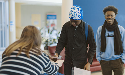 Two students check in to an NSCC event at a table and are handed name badges.