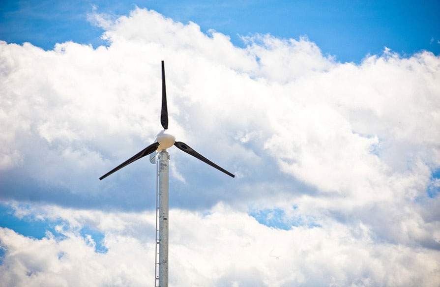 A wind turbine pictured against a bright sky with big, fluffy clouds.