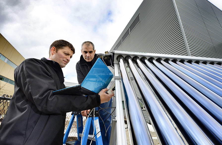 Two NSCC employees looking at a laptop screen near Ivany Campus's outdoor solar classroom.